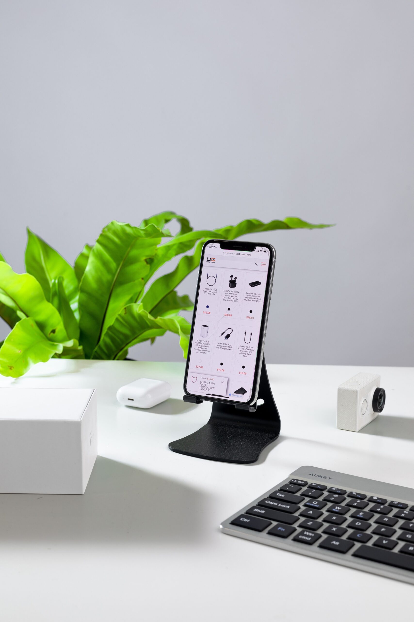 A smartphone on a stand with a keyboard and accessories on a white desk.