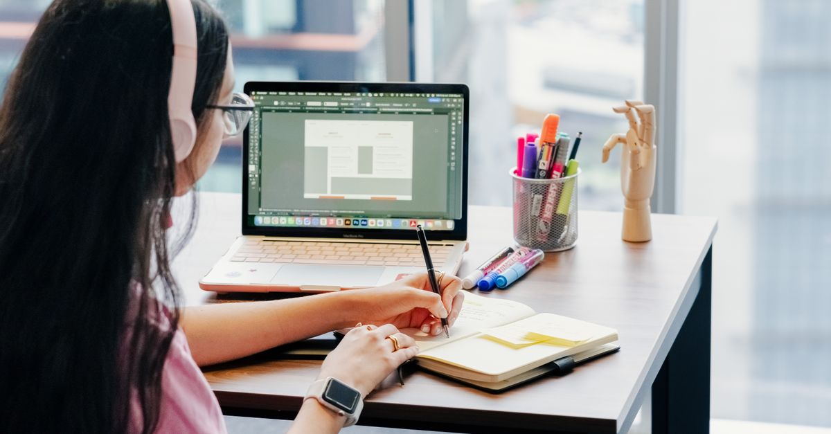 Woman using laptop and notebook in modern home office setup, enhancing productivity.